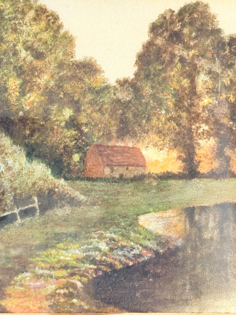 Antique framed rural watercolour of river, trees, and red-roofed building, in dark wooden frame with cream mount, on white surface.