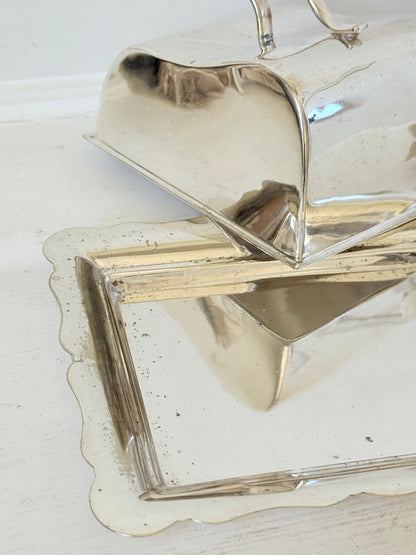 A polished silver serving tray with a scalloped edge and matching lid, shown on a white surface with reflections.