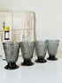 Set of four smoke grey pressed glass footed goblets with a diamond pattern, photographed on a white surface