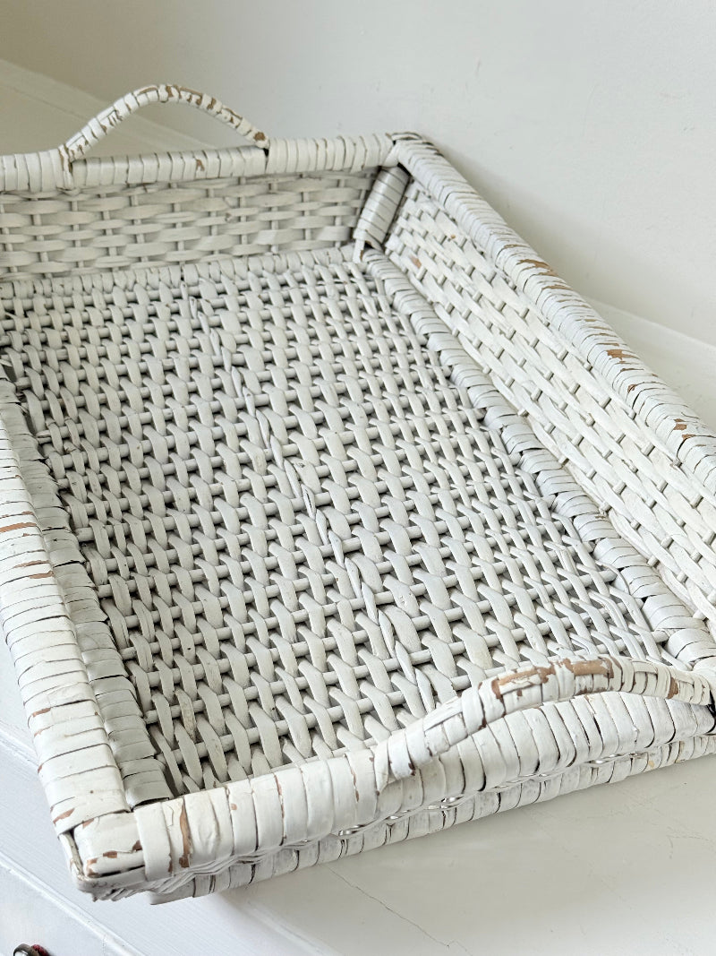 Vintage white painted wicker tray with woven handles photographed on a white surface