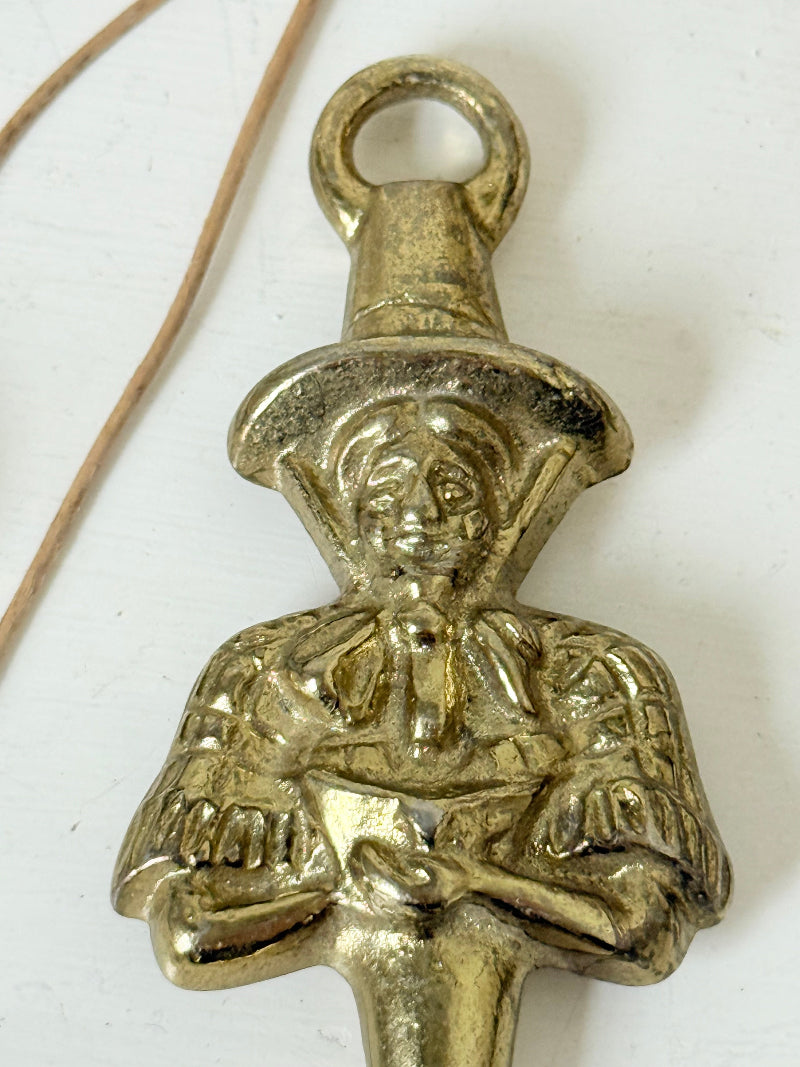 Vintage brass figure bottle opener photographed on a white surface with dried foliage.