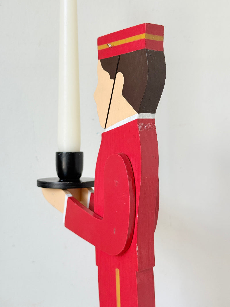 Vintage bellboy candlestick holder in red and black holding a tray with candle, photographed on a white surface