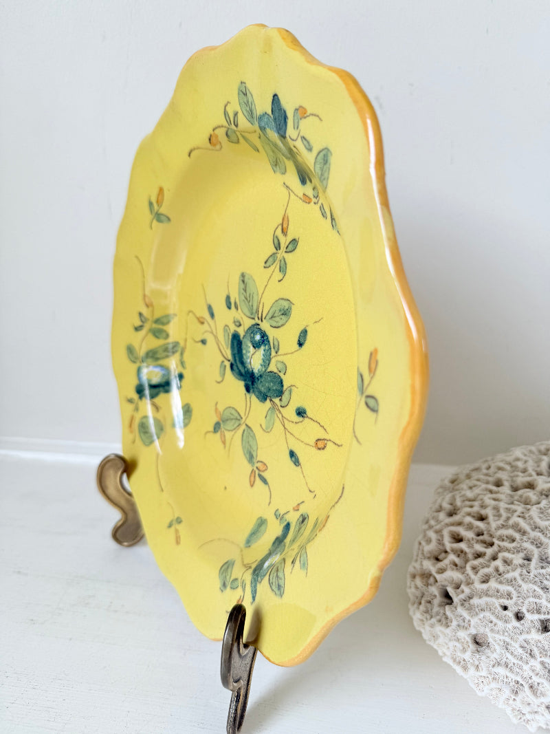 Vintage yellow French faïence plate with scalloped edge and blue floral decoration, photographed on a white surface