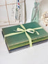 A stack of vintage hardcover books wrapped with a light green and white striped ribbon, styled on a white surface with a glass bottle and dried flowers in the background.