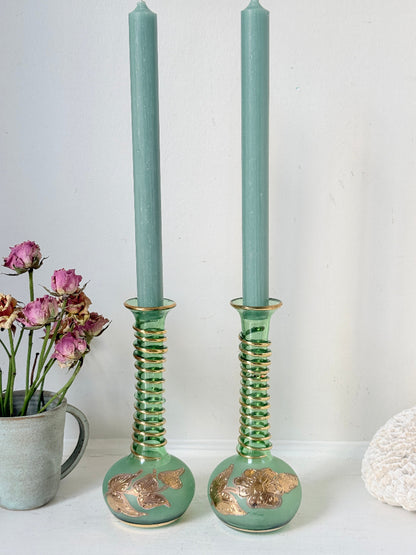 Pair of vintage green glass candlesticks with gold detail and spiral stems styled with blue taper candles on white surface