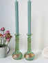 Pair of vintage green glass candlesticks with gold detail and spiral stems styled with blue taper candles on white surface