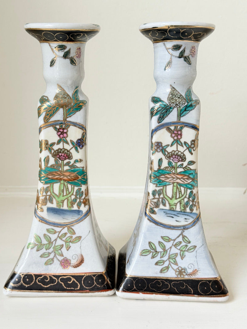 Pair of porcelain candle holders with hand-painted floral and vase motif in muted greens, pinks, and gold, styled with blush pink taper candles.