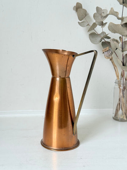 Vintage copper and brass jug with slender handle, photographed on a white surface