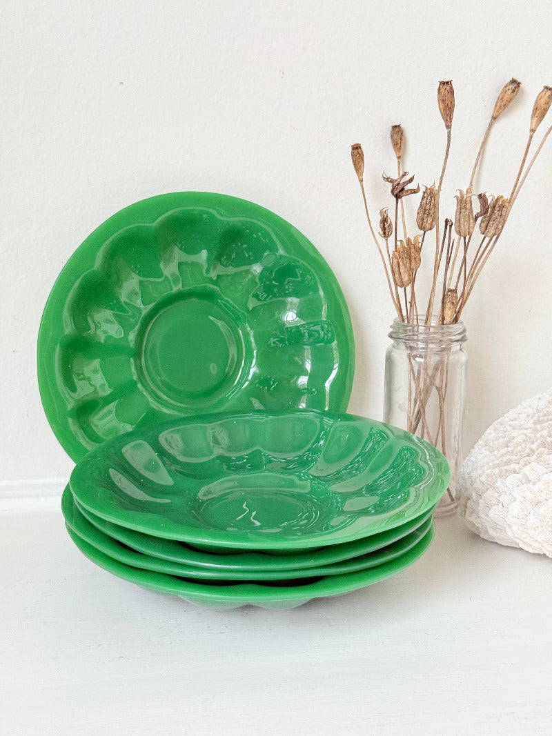 set of five vintage green pressed glass plates with decorative pattern, photographed on a white surface with dried flowers