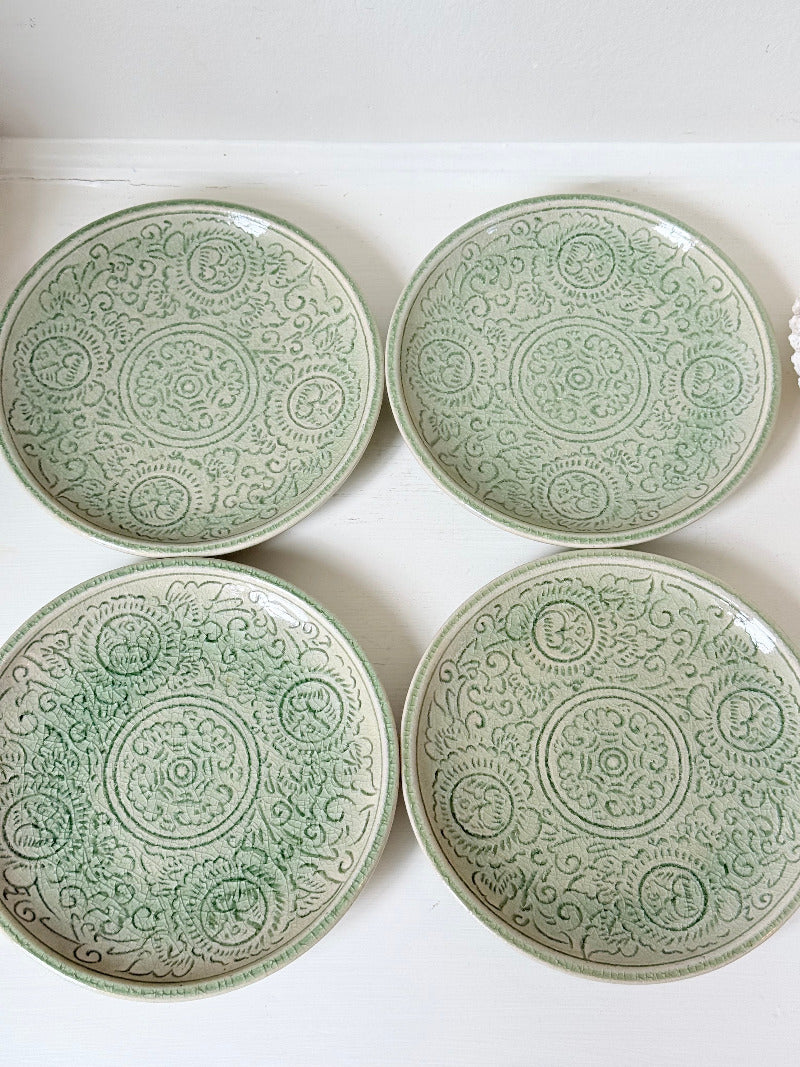 Set of four Thai celadon side plates with embossed patterns and sage green crackled glaze, stacked and photographed on white surface