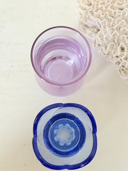 Blue Bormioli Rocco glass candlestick and lilac glass vase photographed on a white surface