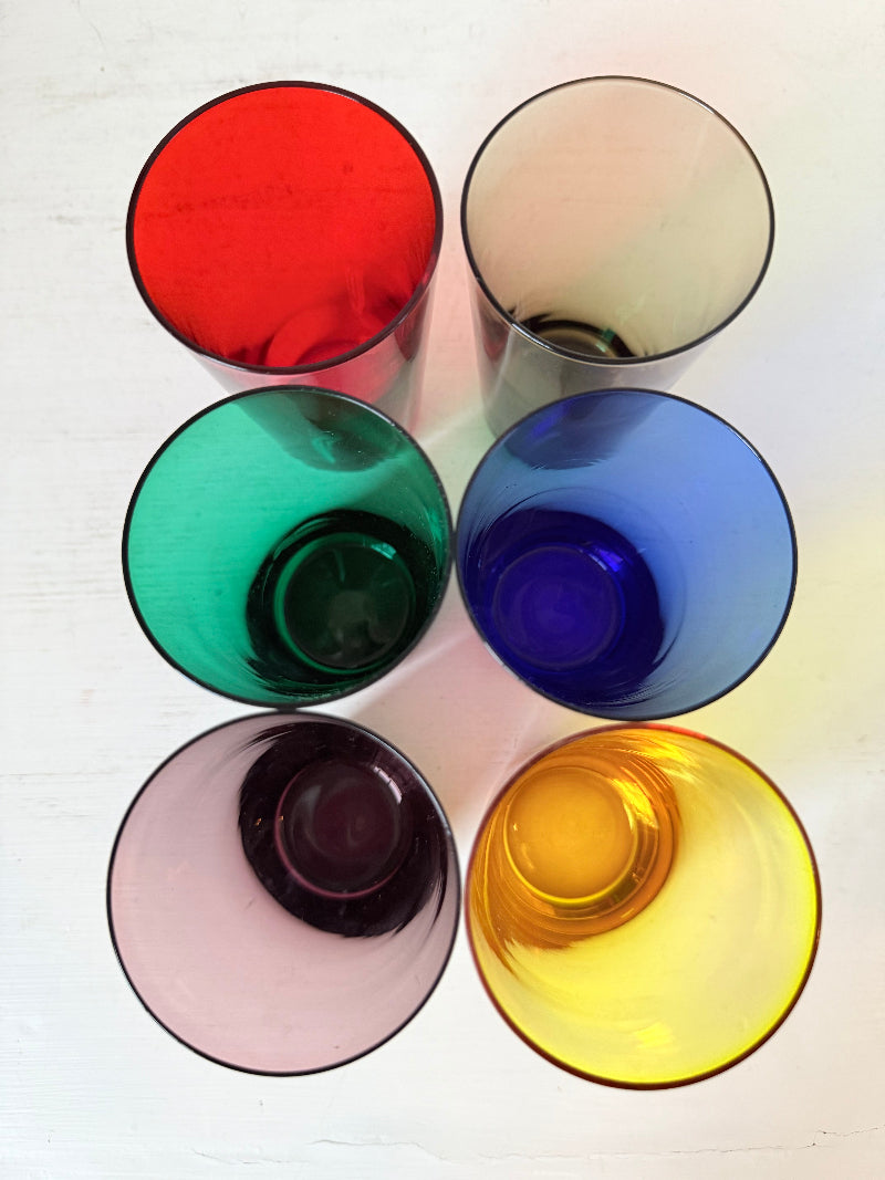 Set of six mid-20th century Boussu coloured glass beakers in rainbow hues, green with original label, photographed on white surface.