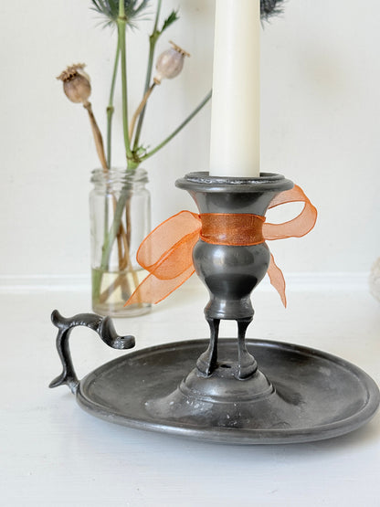 Vintage pewter chamberstick with handle and circular tray, photographed on a white surface