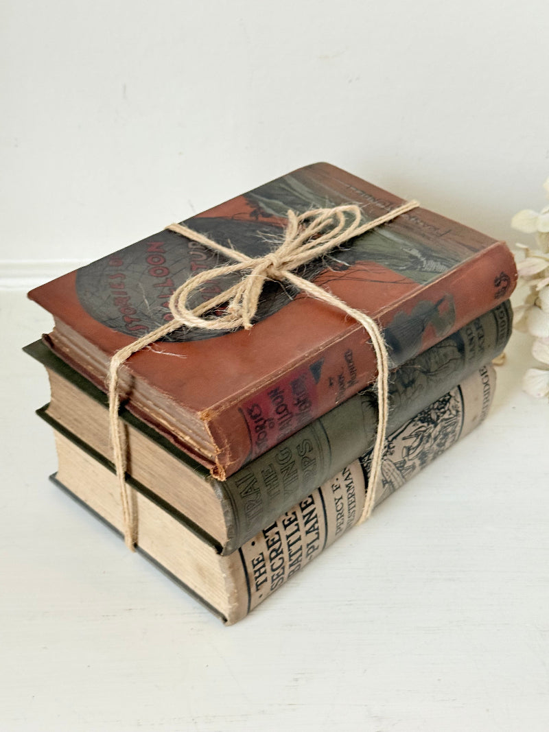 Vintage decorative book bundle in red, olive green and cream tied with twine, photographed on a white surface