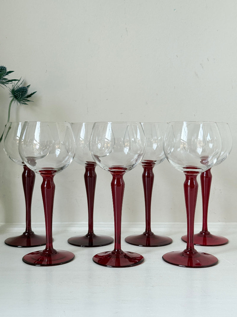 Set of seven vintage wine glasses with clear bowls and red stems, photographed on a white surface