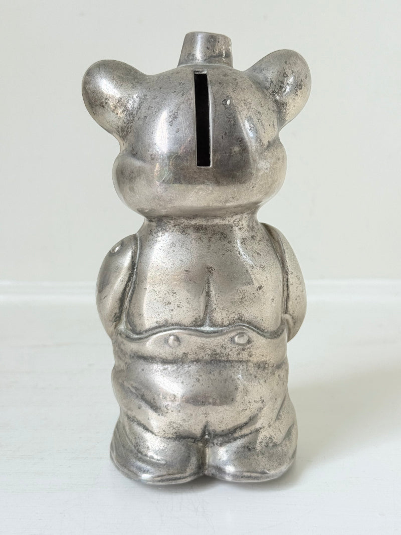 Vintage silver tone metal bear money box with coin slot on top, photographed on a white surface.