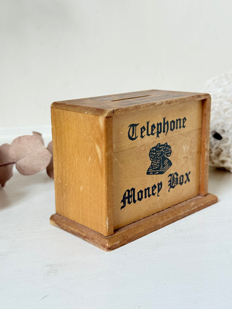 Vintage wooden telephone money box with printed lettering, photographed on a white surface