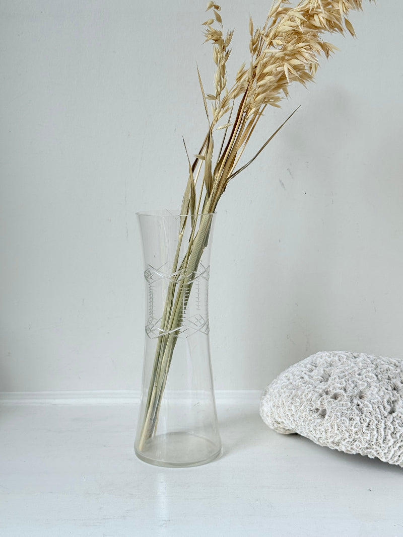 Vintage clear glass cylinder vase with etched leaf design, photographed on a white surface.
