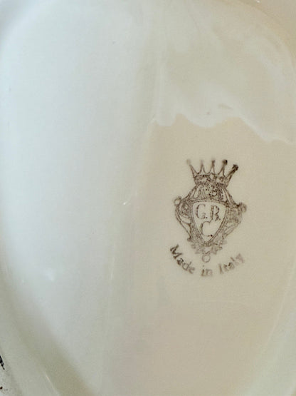 Italian ceramic dish featuring two white dogs on a sculpted leaf base, photographed on a white surface.