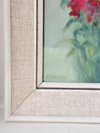 Close-up of a framed floral painting corner showing a textured off-white linen frame, a white painted frame edge, and part of the artwork with red flowers and green leaves.