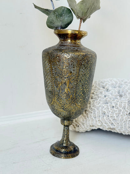 Indian Benares brass chalice vase with figural panels and pedestal base, photographed on a white surface