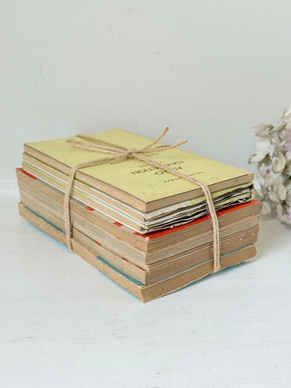 Bundle of vintage Penguin paperback books in orange and cream tones tied with twine, photographed on a white surface