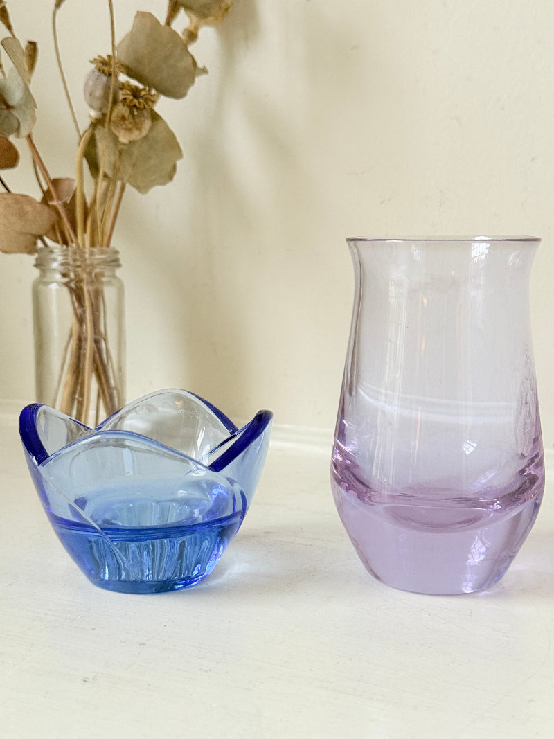 Blue Bormioli Rocco glass candlestick and lilac glass vase photographed on a white surface