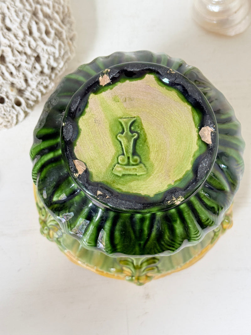 An antique green glazed ceramic bowl viewed from underneath, showing a light green interior with a central monogram and dark green fluted rim.