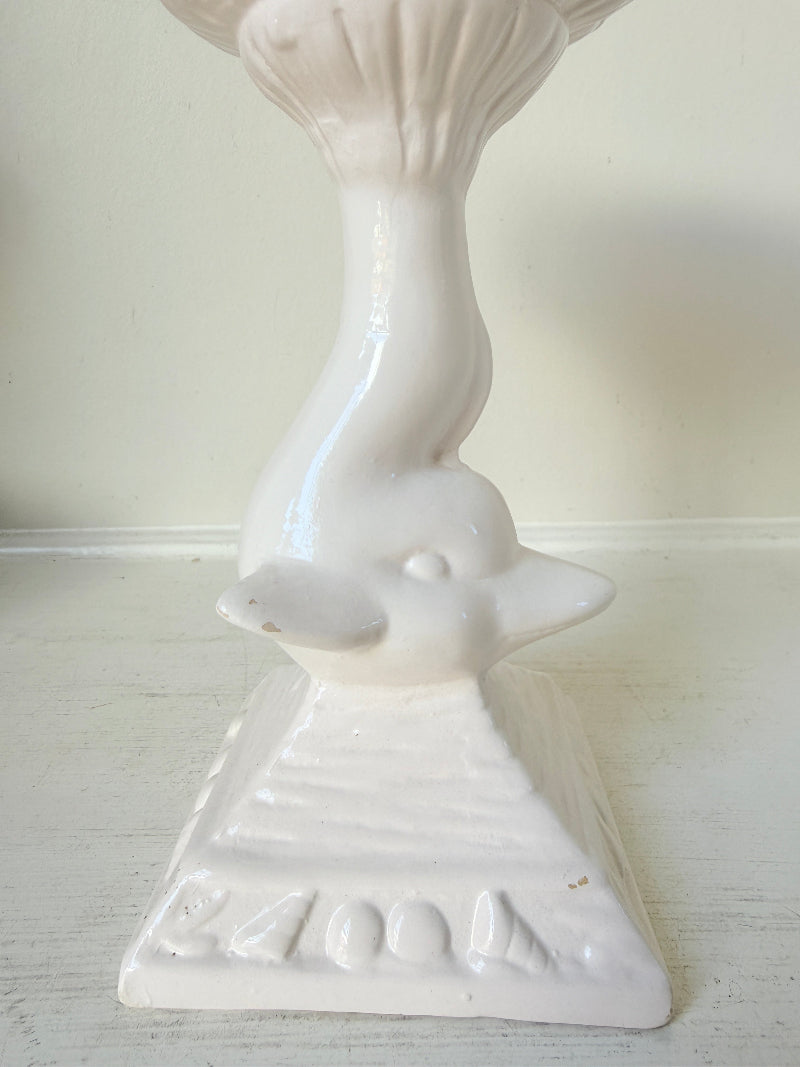 A white ceramic bird-shaped candlestick holder with a pedestal base, photographed against a plain off-white wall and surface.