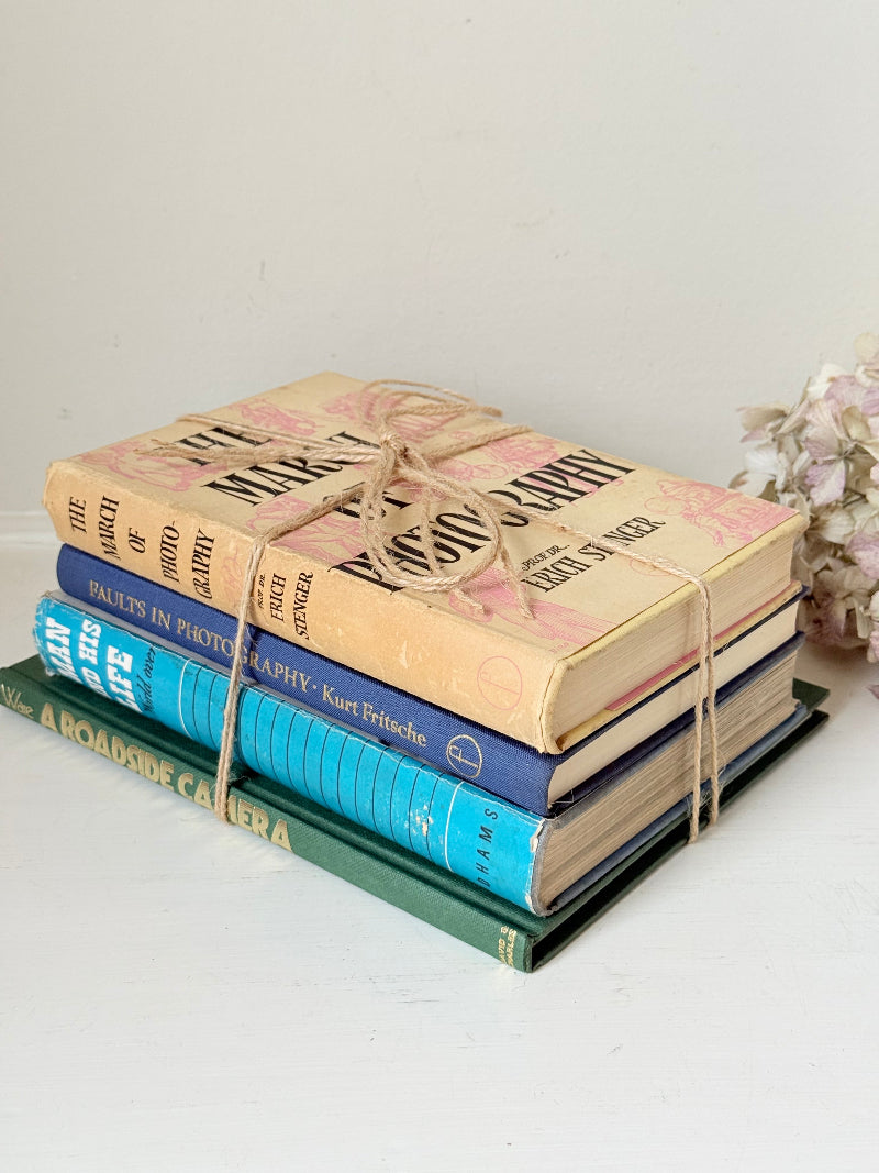 Bundle of vintage books in blue and neutral tones tied with twine, photographed on a white surface