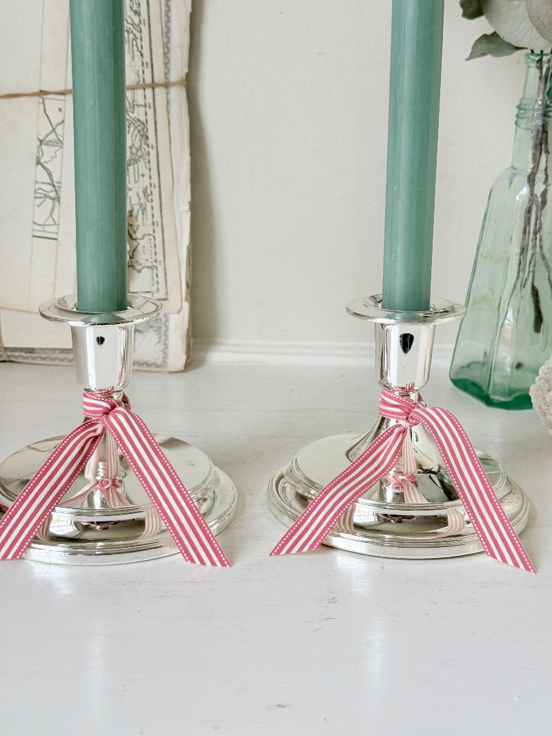 Pair of silver tone candlesticks with wide round stepped bases holding green candles, photographed on a white surface