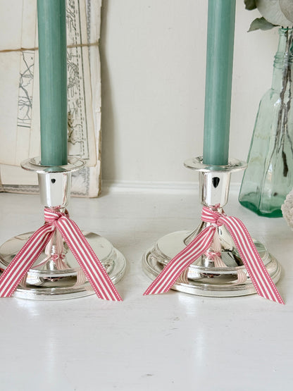 Pair of silver tone candlesticks with wide round stepped bases holding green candles, photographed on a white surface