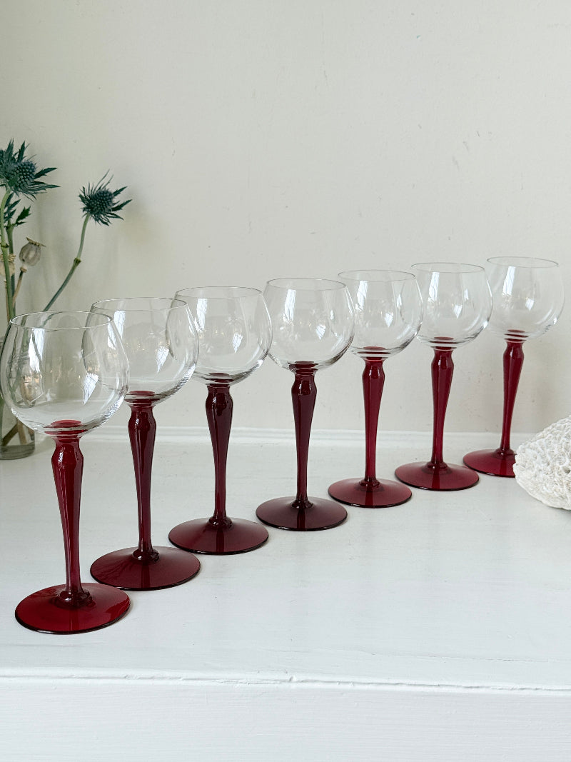 Set of seven vintage wine glasses with clear bowls and red stems, photographed on a white surface