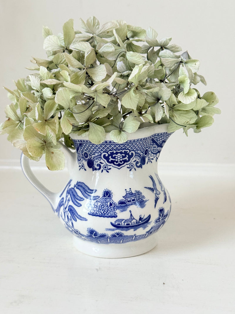 Vintage Churchill Blue Willow milk jug in blue and white ceramic photographed on a white surface.