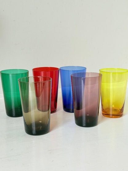Set of six mid-20th century Boussu coloured glass beakers in rainbow hues, green with original label, photographed on white surface.