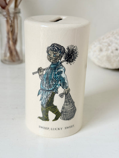 Vintage ceramic money box with illustrated figures photographed on a white surface