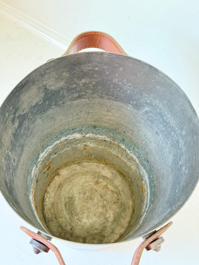 Vintage metal wine cooler with leather handles and tapered form, photographed on white surface.