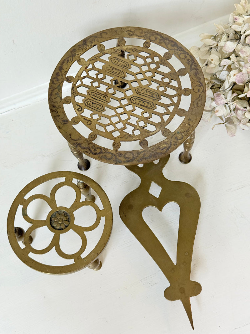 Vintage brass trivet trio with ornate cutwork designs and aged patina, photographed on a white surface