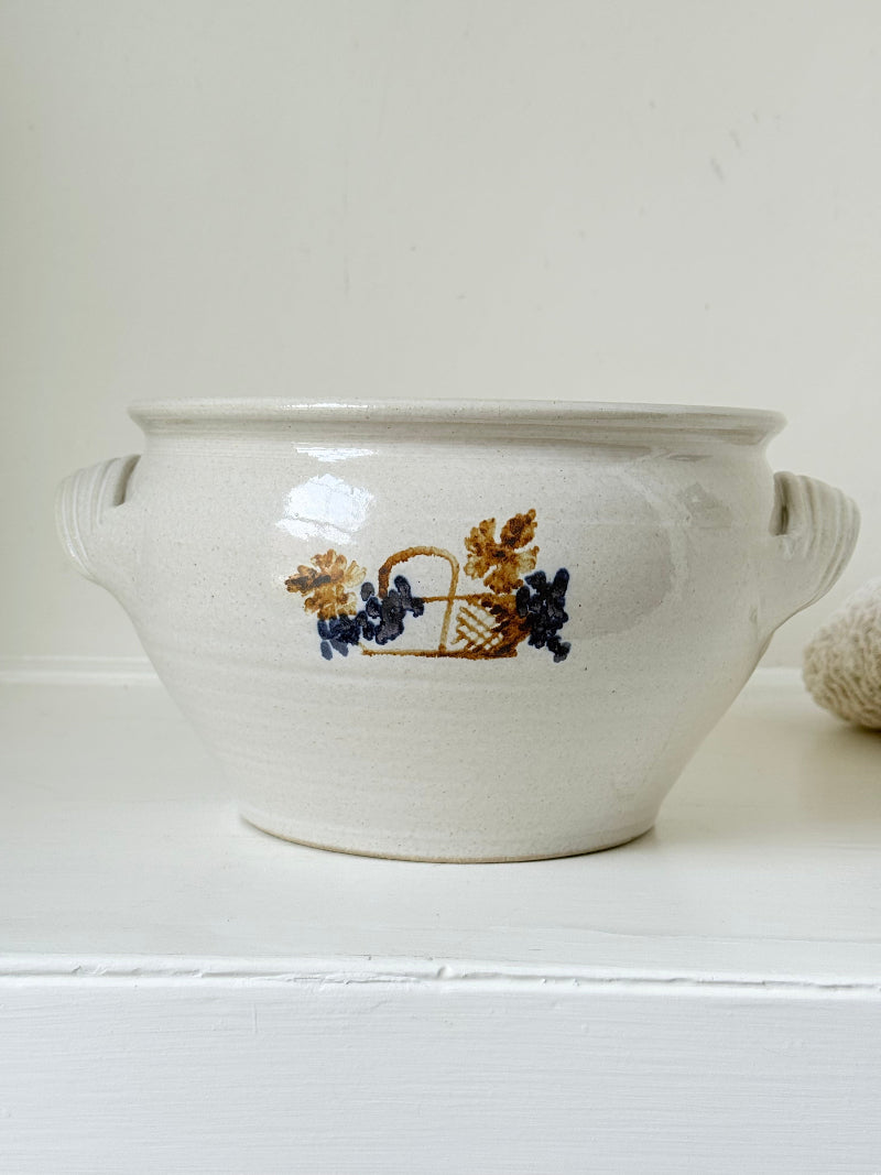 Large studio pottery bowl with hand-painted grape motif and side handles, photographed on a white surface