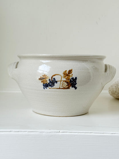 Large studio pottery bowl with hand-painted grape motif and side handles, photographed on a white surface