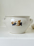 Large studio pottery bowl with hand-painted grape motif and side handles, photographed on a white surface