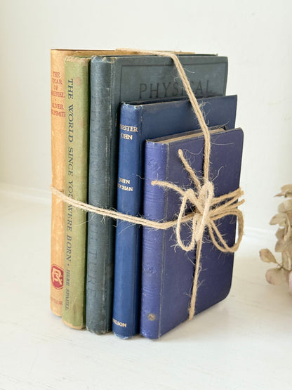Vintage decorative book bundle in blue and green tied with twine, photographed on a white surface