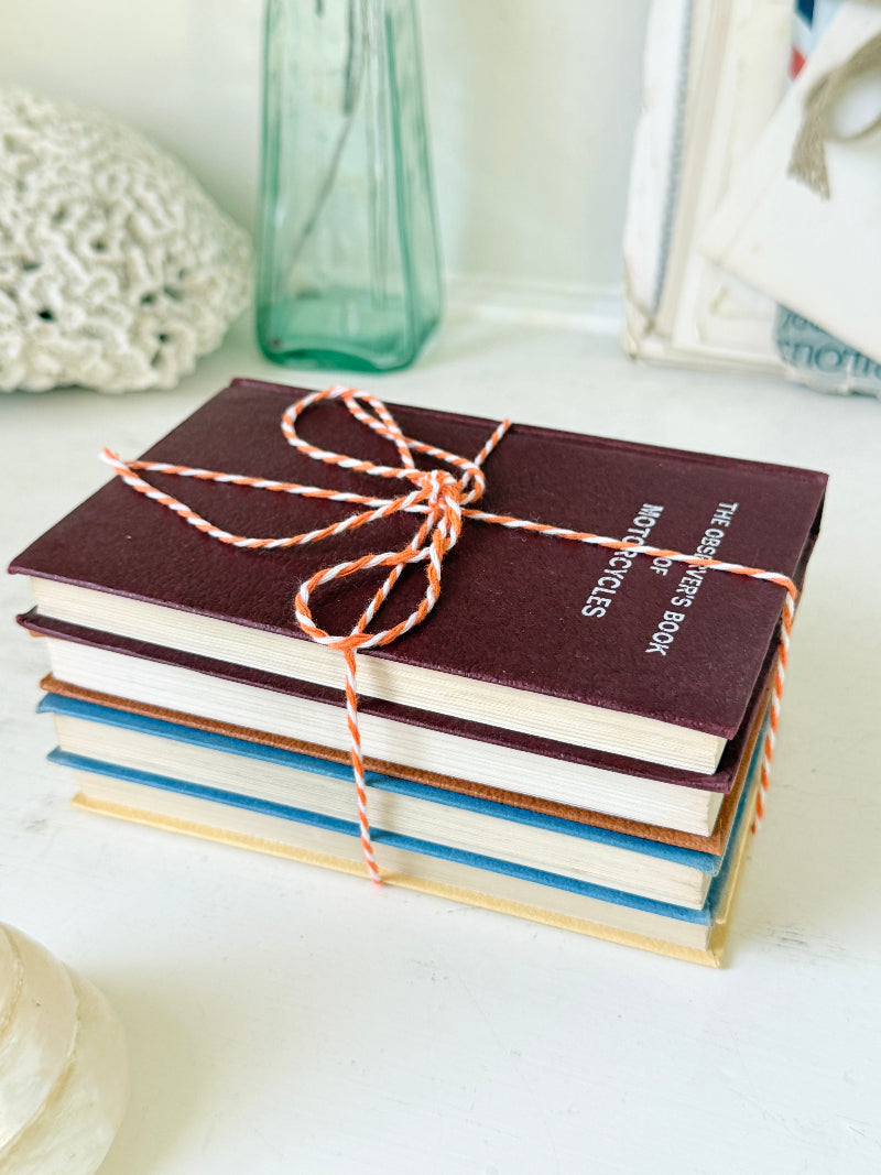 A stack of hardcover notebooks tied with orange-and-white striped string, with the top notebook reading &