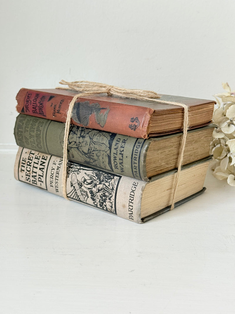 Vintage decorative book bundle in red, olive green and cream tied with twine, photographed on a white surface