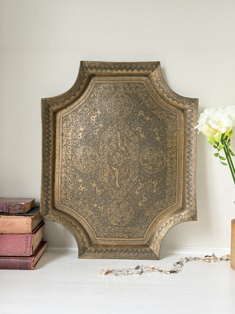 Vintage hand engraved brass wall plaque with floral scrollwork, figural decoration, shaped edge and aged patina