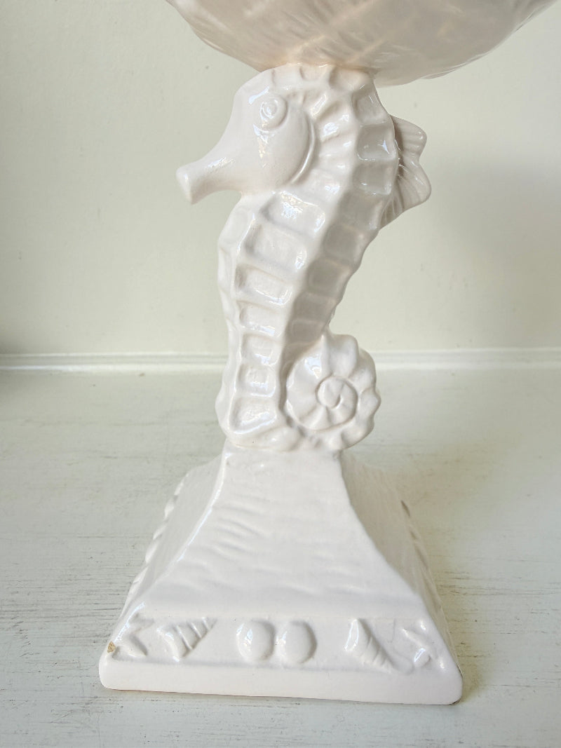 A white ceramic seahorse-shaped pedestal stand with a textured base and a matching bowl on top, photographed against a plain off-white background.