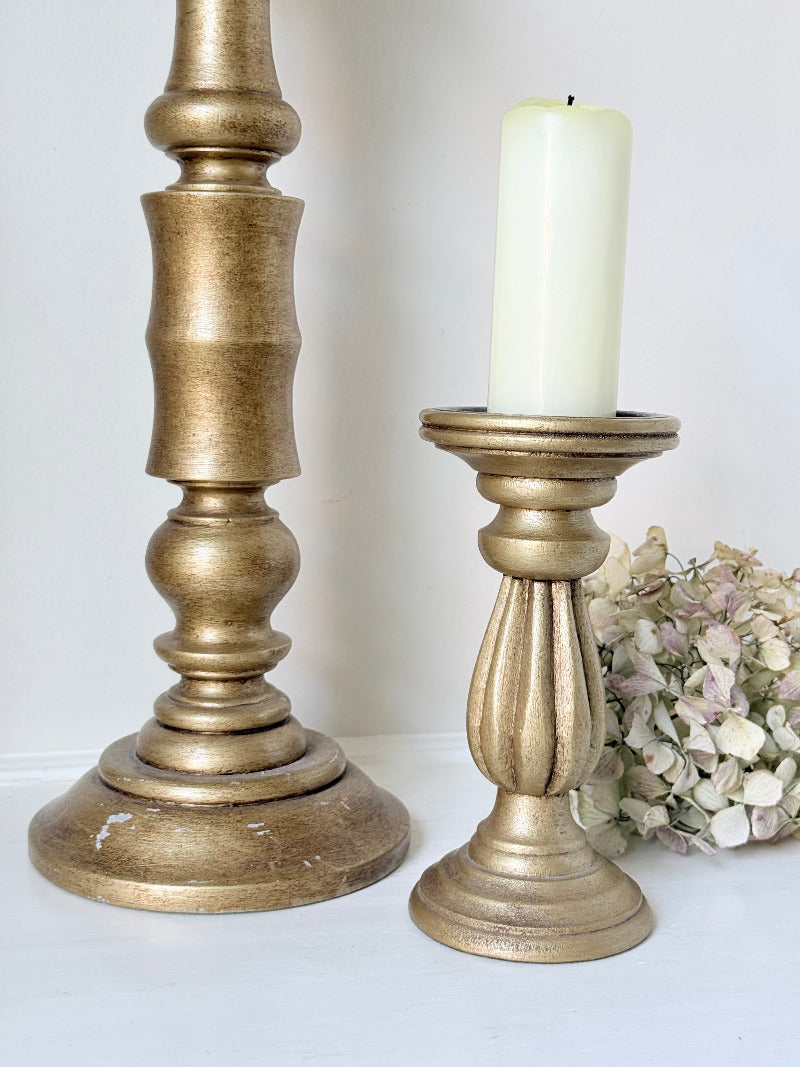 Pair of vintage wooden candlesticks, one tall and one small, in golden-toned finish, styled with pillar candles on a white surface.