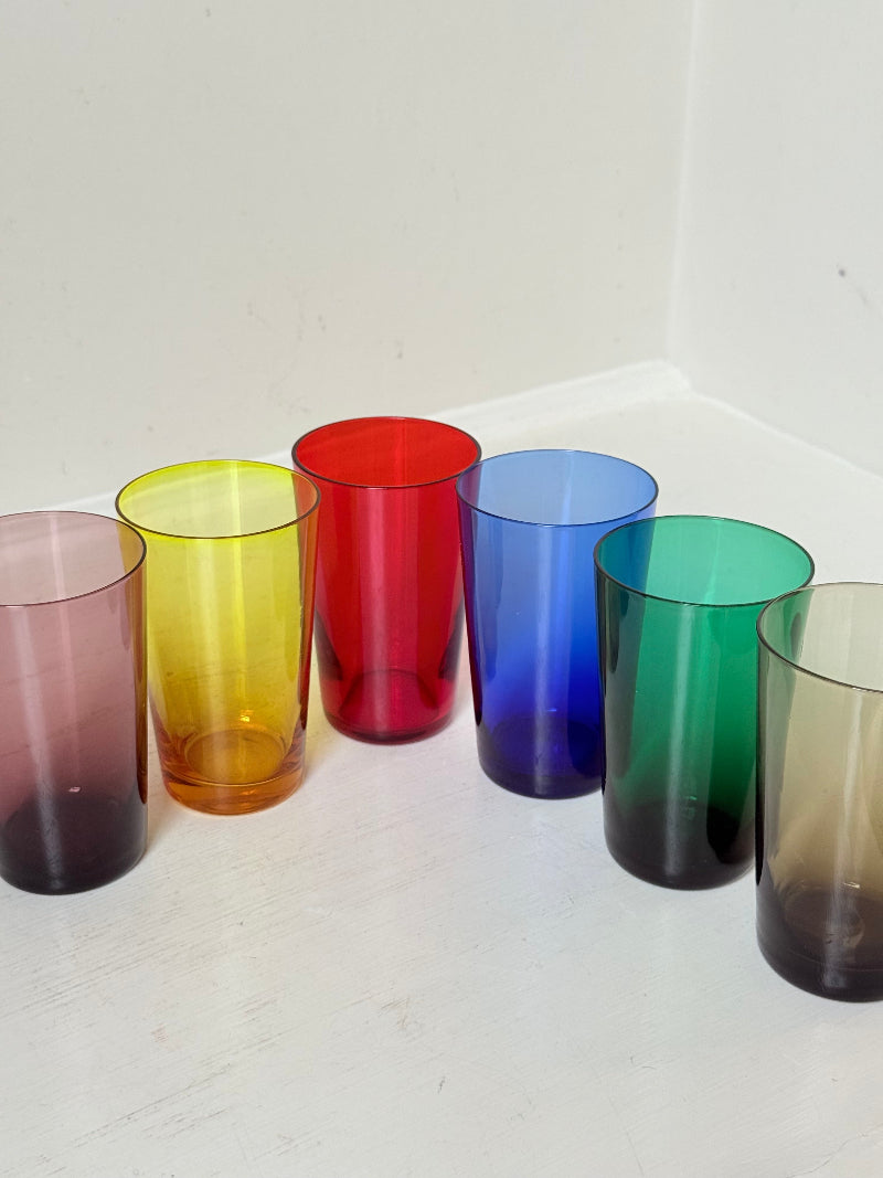Set of six mid-20th century Boussu coloured glass beakers in rainbow hues, green with original label, photographed on white surface.