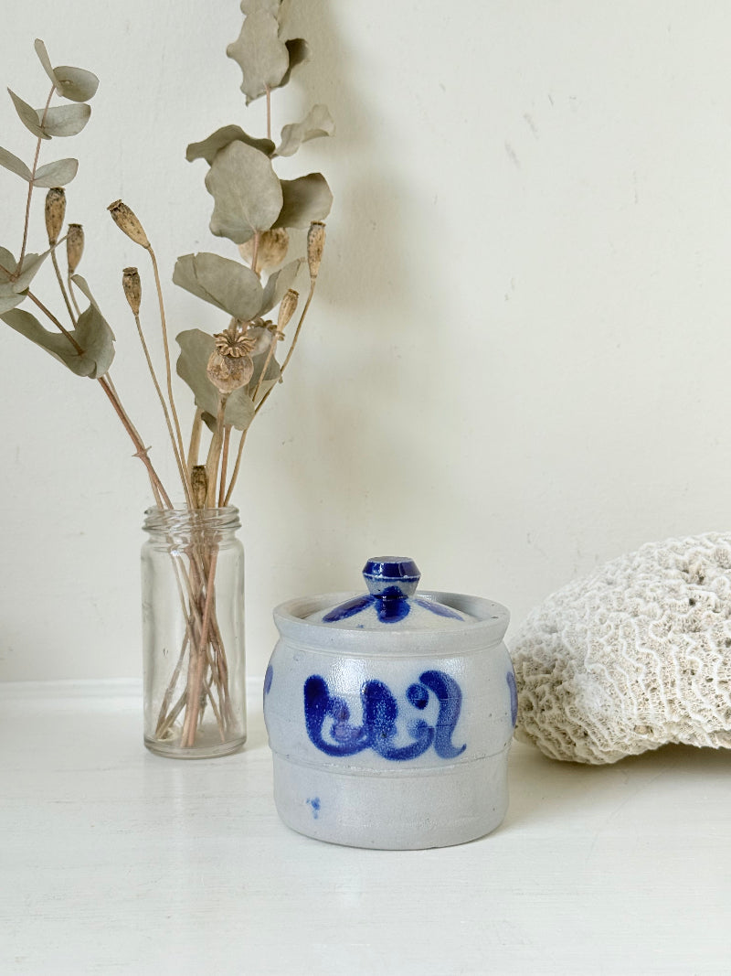 Vintage lidded pottery jar with hand painted blue floral decoration, photographed on a white surface