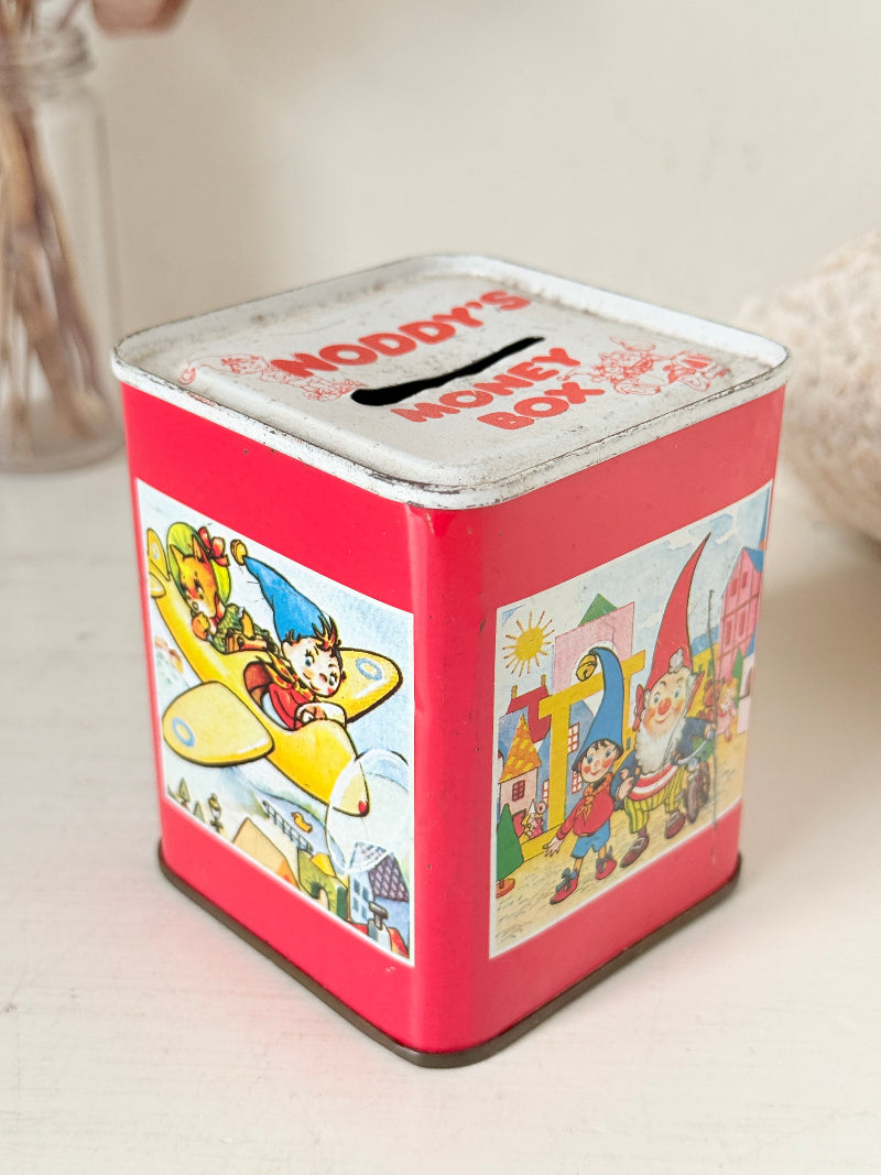 Vintage Noddy money box tin in red with illustrated panels, photographed on a white surface